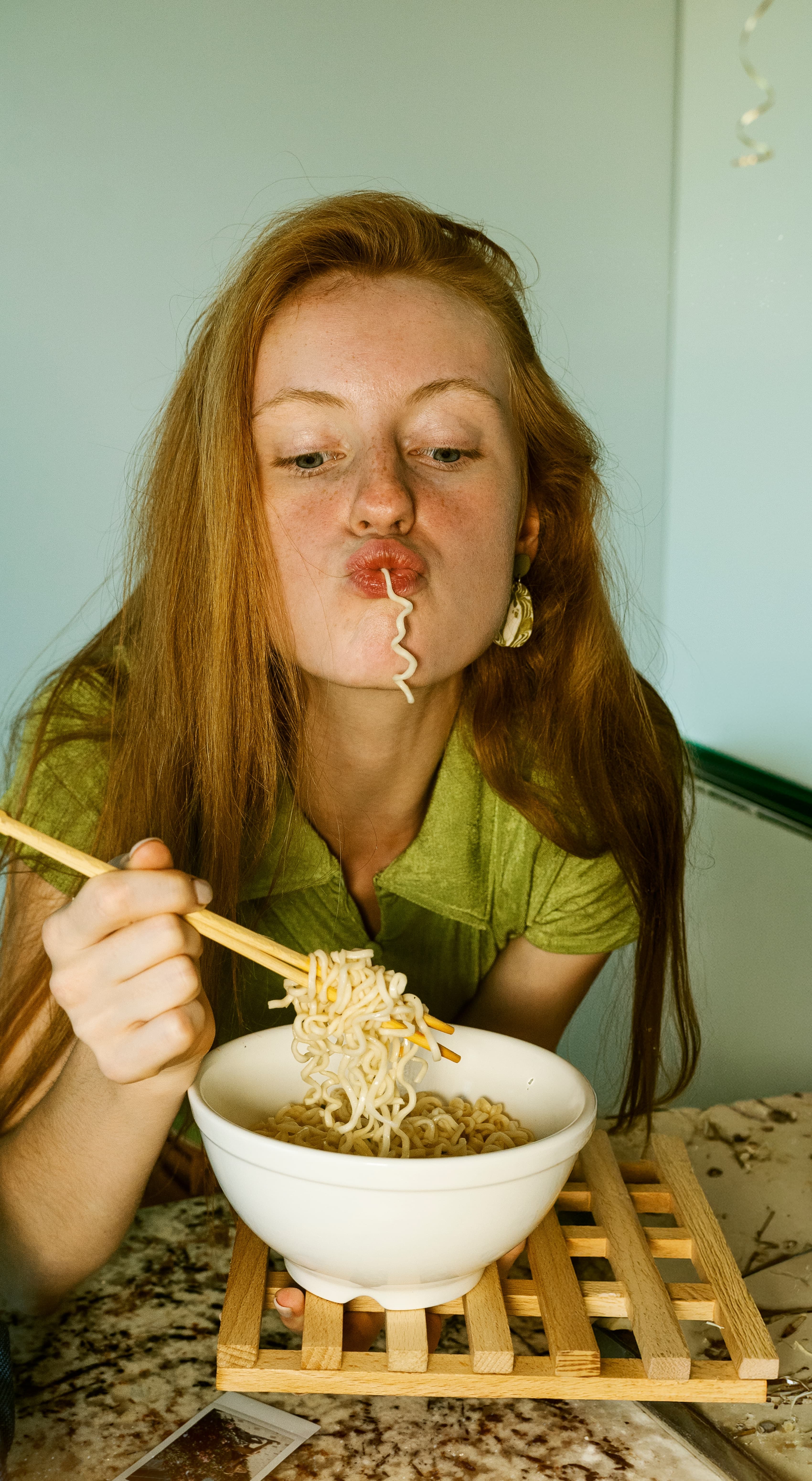 Una ragazza con i capelli rossi mangia con le bacchette una ciotola di noodles senza glutine