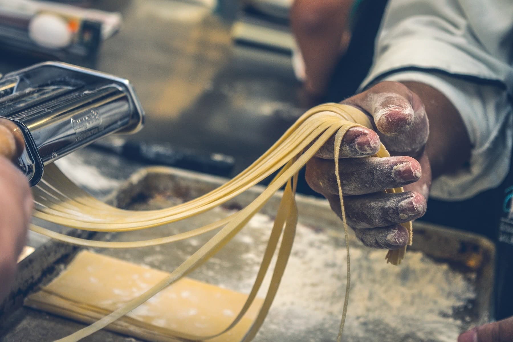 Mani infarinate che lavorano la pasta fresca appena tirata